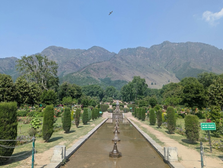 A Mughal garden in Srinagar with fountains, trees, and mountain views